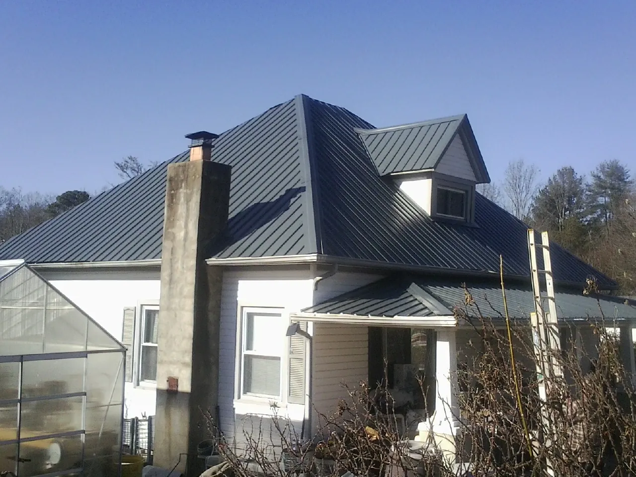 Dark blue standing seam metal roof on a white farmhouse with dormer — Slate & Tile Roof Repair by Roofing Brothers in Rowlett