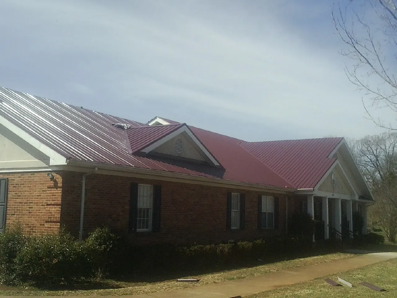 Red metal roof with gabled entries on a long brick building, from a Hail Damage Roof Repair job in Rowlett