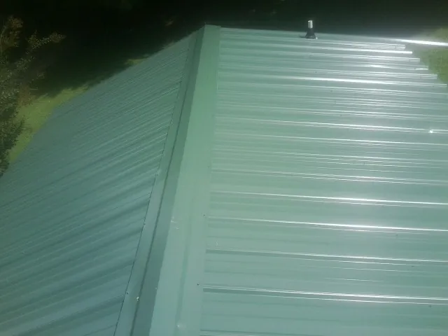 New green metal panels meeting at the ridge of a roof — Flat Roof Repair work by our crew in Rowlett