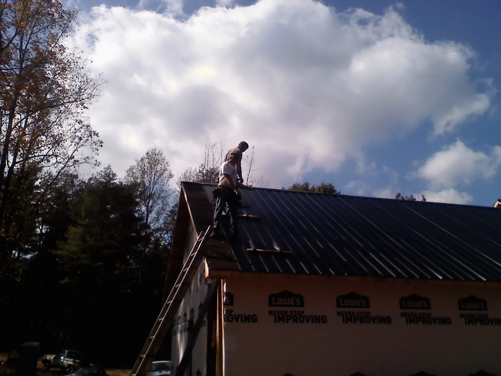 Roofer fastening dark metal panels high against a cloudy sky, from a Roof Inspection job in Rowlett